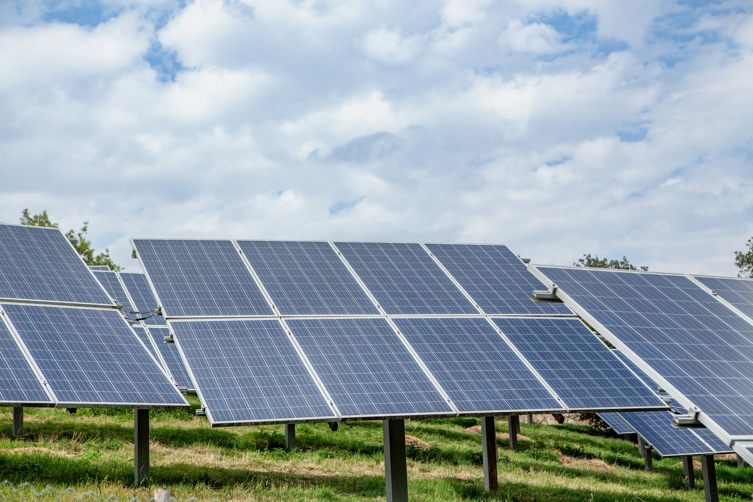 Rows of solar panels in a field beneath clouds.